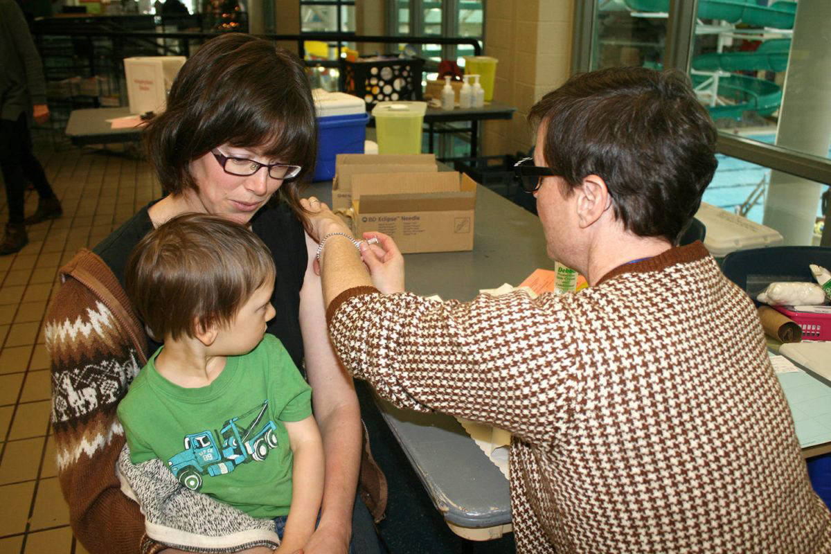 Public health nurse Lisa Halliwell gives a flu shot to Danielle Wonderham while her two-year-old son Evan patiently waits his turn at Thursday’s clinic at Saanich Commonwealth Place. Dan Ebenal/Black Press