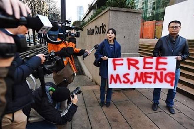 People hold a sign at a B.C. courthouse prior to the bail hearing for Meng Wanzhou, Huawei’s chief financial officer on Monday, December 10, 2018. THE CANADIAN PRESS/Jonathan Hayward