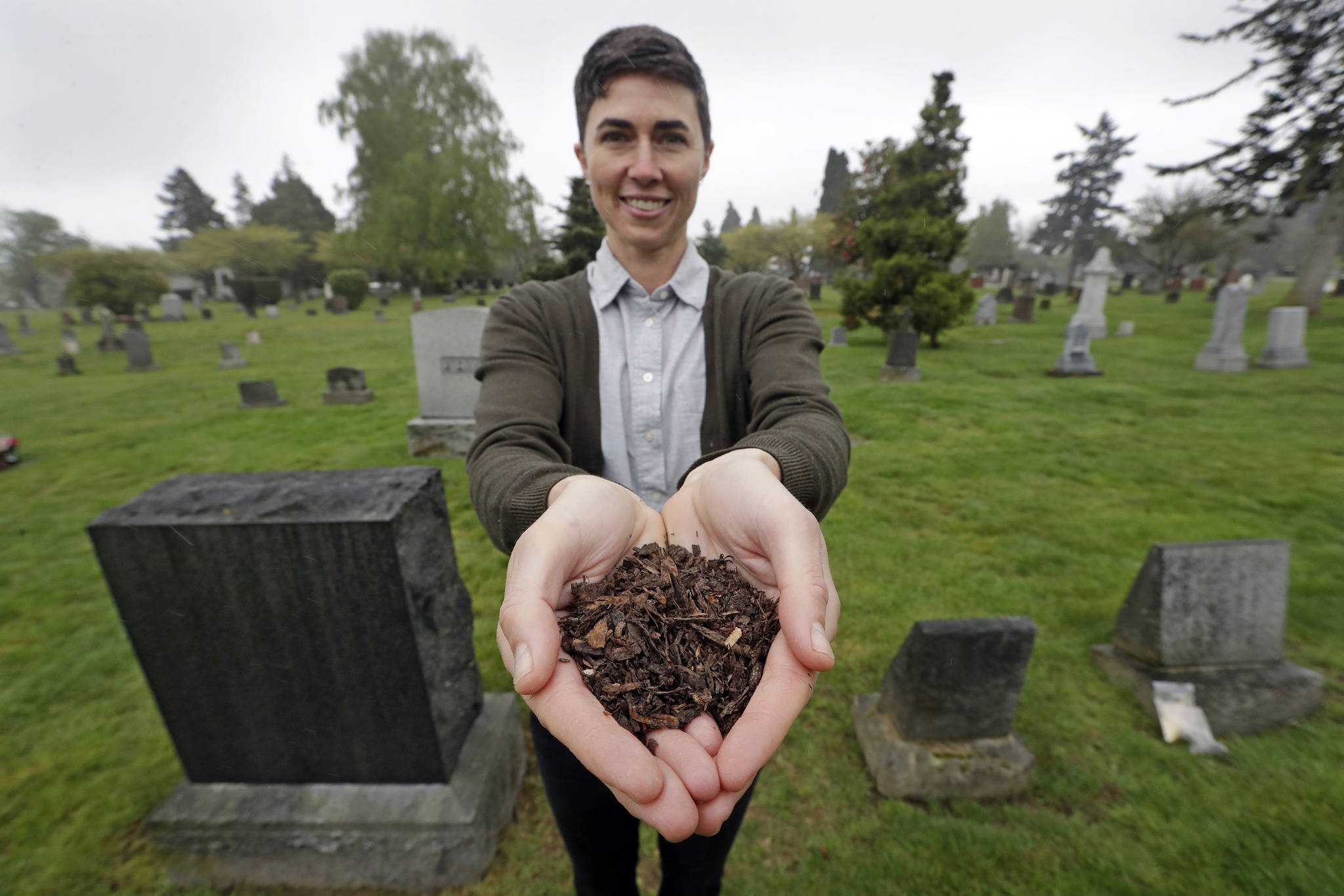 In this Friday, April 19, 2019, photo Katrina Spade, the founder and CEO of Recompose, displays a sample of the compost material left from the decomposition of a cow, using a combination of wood chips, alfalfa and straw, as she poses in a cemetery in Seattle. Washington is set to become the first state to allow the burial alternative known as “natural organic reduction,” that turns a body into soil in a matter of weeks. (AP Photo/Elaine Thompson)