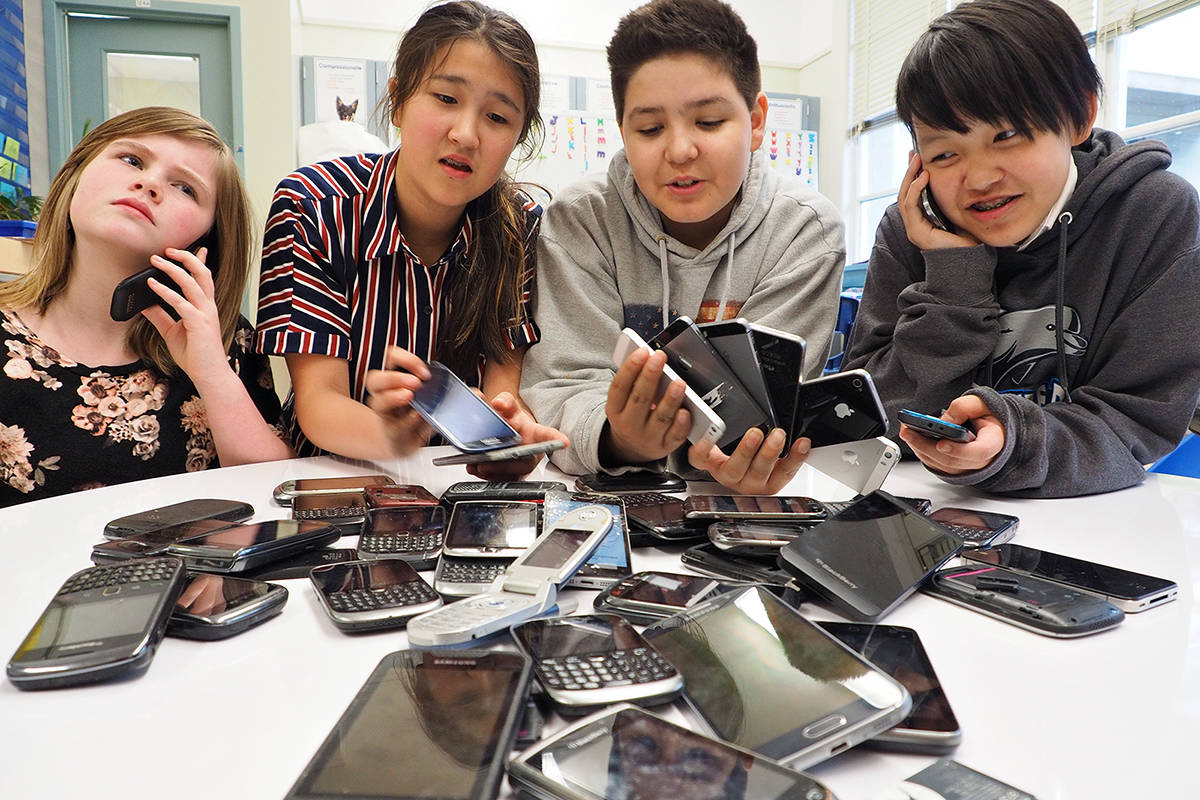 Departure Bay Elementary Eco-School students Carly Sigmundson, left, Alex Nelson, Marcus Bertrand and Helena Cowles check out the variety of smartphones and flip phones that have been donated so far for an environmental initiative and fundraiser. (CHRIS BUSH/News Bulletin)