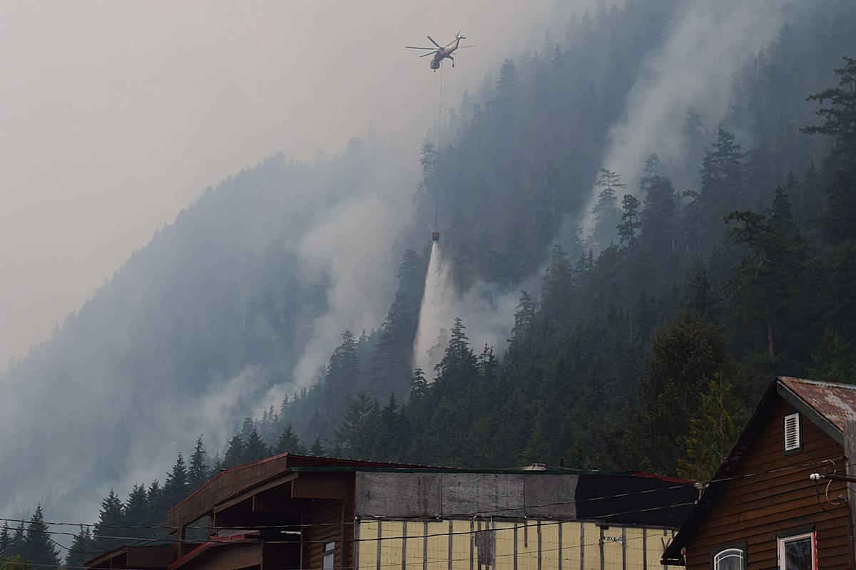 A helicopter buckets wildfires as smoke rises from the mountains surrounding Zeballos in an Aug. 17, 2018 file photo.