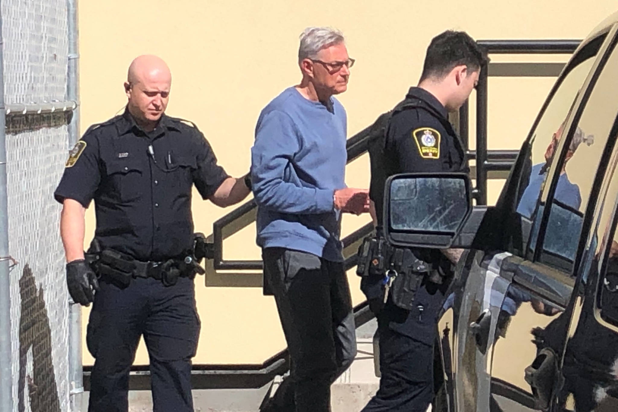 John Brittain, 68, being escorted into the Penticton courthouse in April. Brittain and his ex-wife, Katherine Brittain, have been named in a civil lawsuit by the daughter of a couple that were fatally shot. (Western News file photo)