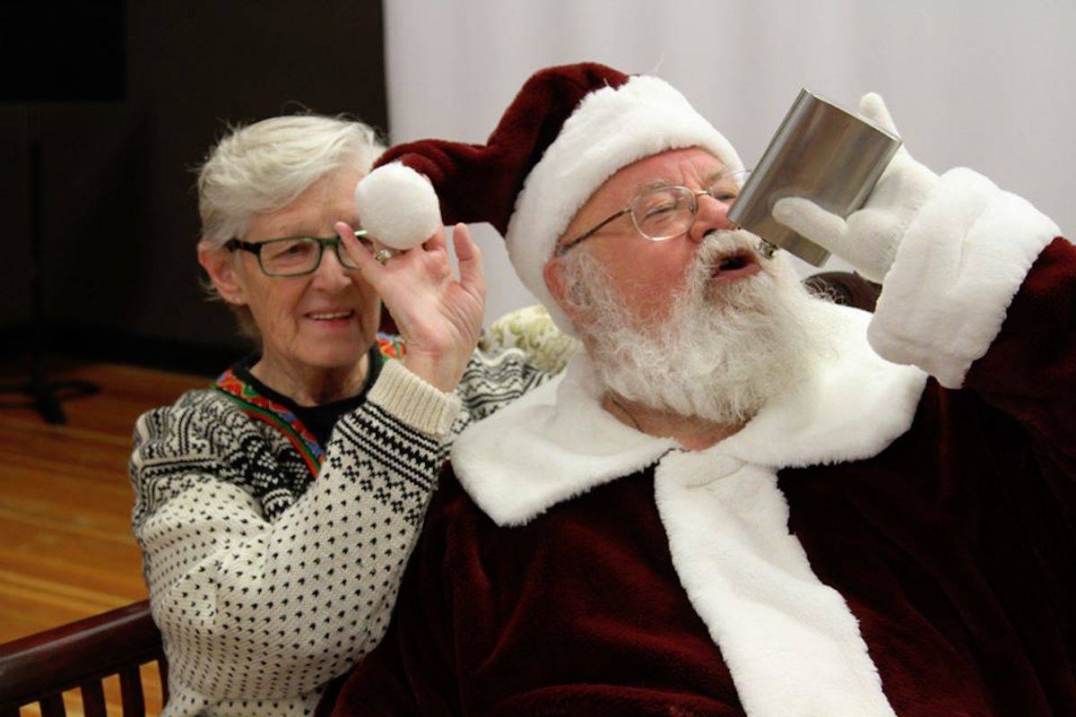 Gary Haupt (right) dressed as Santa at a recent Christmas market at Penticton’s Shatford Centre takes a silly photo with a woman who asked him to pretend to drink from a flask. This is one of the photos on Haupt’s personal Facebook page that landed him in hot water with the Cherry Lane Shopping Centre, which decided to terminate his upcoming contract as their mall Santa. (Photo from Facebook)