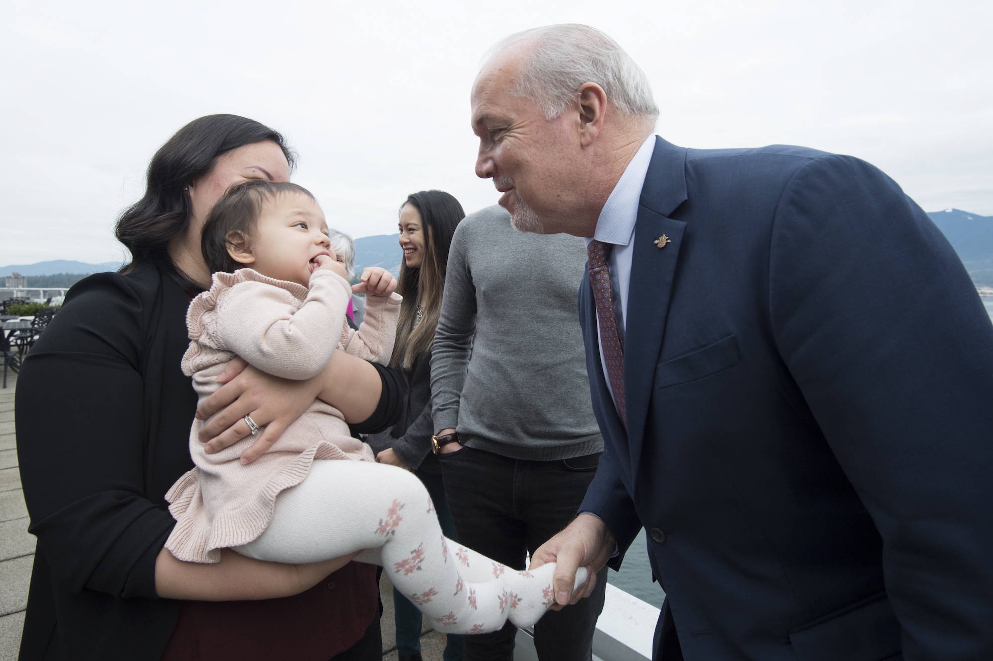 Premier John Horgan shakes thirteen-month-old Caliah Kornneluk’s foot as her mom Jocye Yan looks on after the premier along with Minister of Finance, Carole James and Minister of Health, Adrian Dix held a news conference in downtown Vancouver, Thursday, December, 5, 2019. THE CANADIAN PRESS/Jonathan Hayward