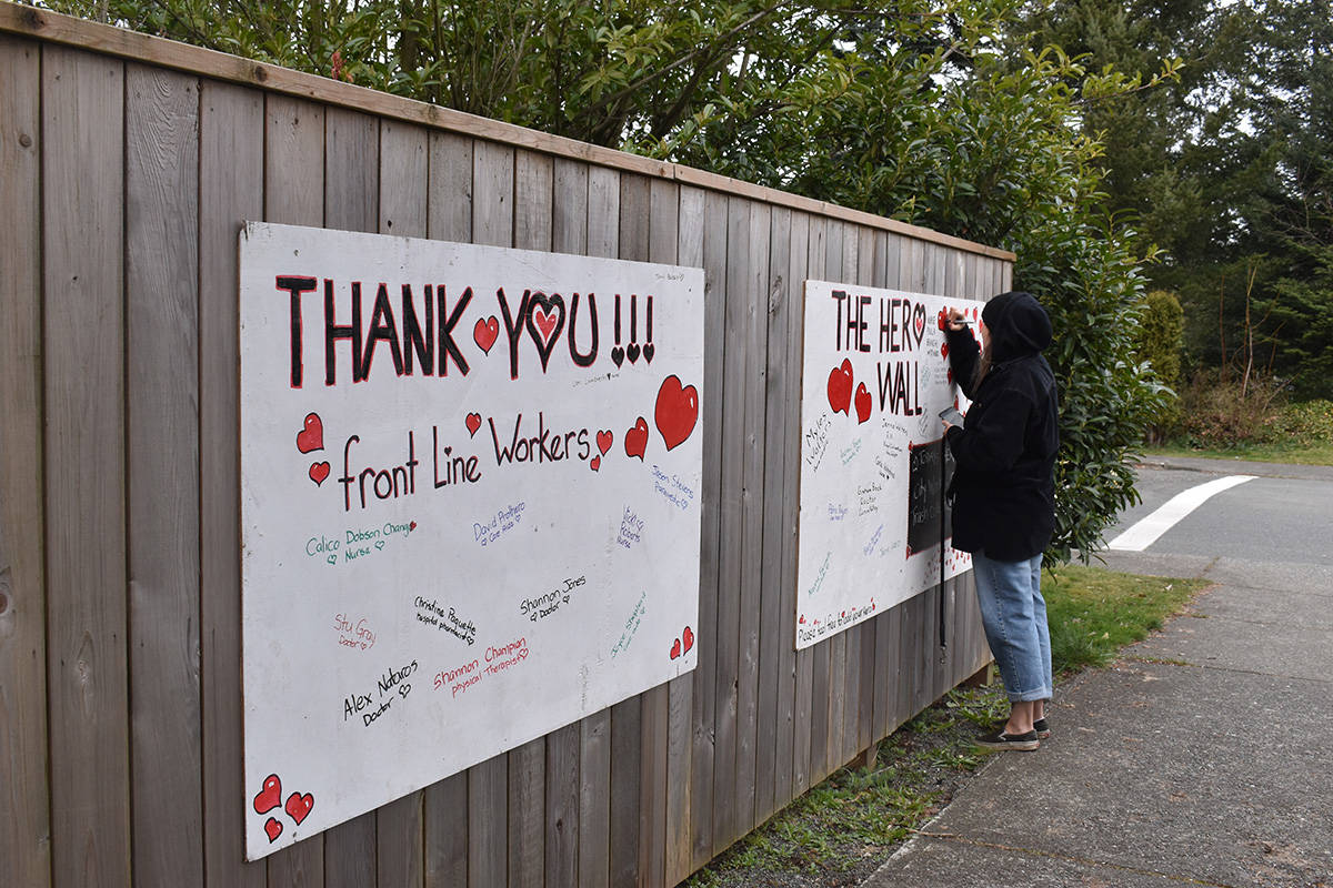 Kira Marshall adds a name to the Hero Wall erected on a fence at the corner of Cliffe Avenue and First Street in Courtenay. Photo by Terry Farrell