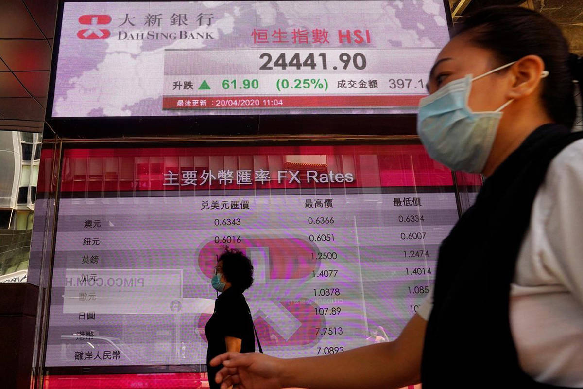 People wearing face masks walk past a bank electronic board showing the Hong Kong share index at Hong Kong Stock Exchange Monday, April 20, 2020. Shares were mixed in Asia on Monday, while oil prices have fallen back. (AP Photo/Vincent Yu)