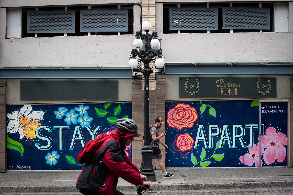 A pedestrian and cyclist pass a closed business with a mural that says ‘Stay Apart’ on the boarded up windows, in downtown Vancouver, on Sunday, April 19, 2020. THE CANADIAN PRESS/Darryl Dyck