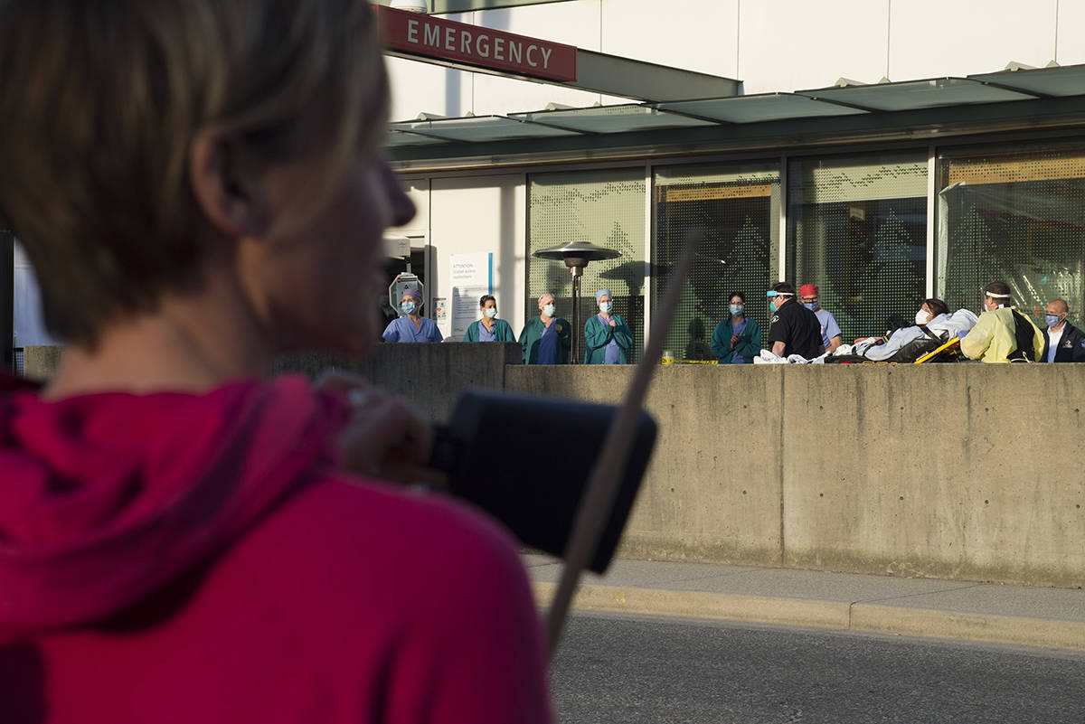 A woman hits a cow bell with a drum stick as a part of the 7pm tribute to health-care workers outside the Lions Gate Hospital in North Vancouver, B.C. Wednesday, April 8, 2020. THE CANADIAN PRESS/Jonathan Hayward
