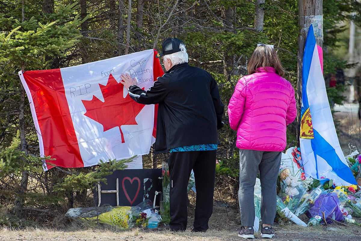 A couple place a flag at a memorial in Portapique, N.S. on Wednesday, April 22, 2020. RCMP say at least 22 people are dead after a man who at one point wore a police uniform and drove a mock-up cruiser, went on a murder rampage in Portapique and several other Nova Scotia communities. THE CANADIAN PRESS/Andrew Vaughan