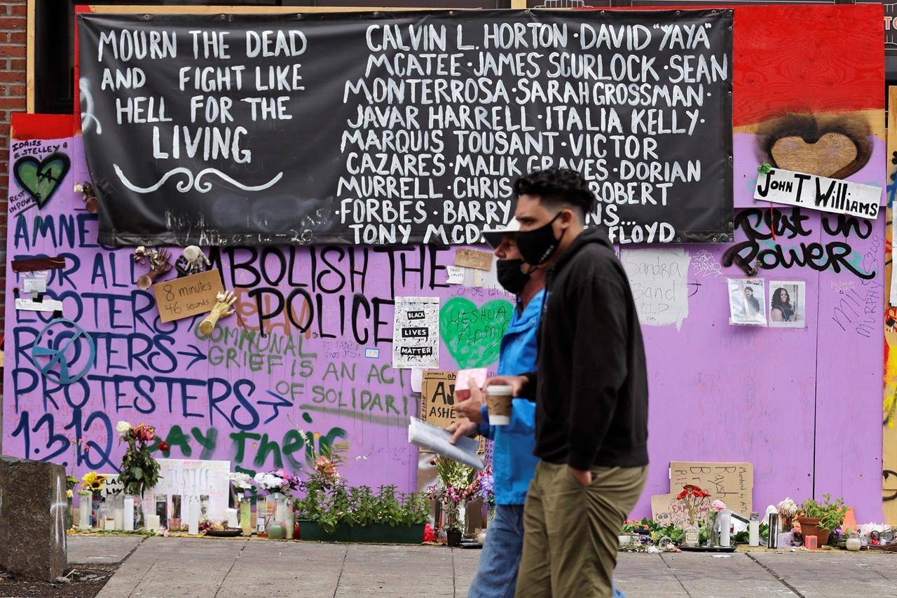 Two people walk past a memorial Sunday, June 28, 2020, in Seattle, for people of color believed to have died in police custody, where several streets are blocked off in what has been named the Capitol Hill Occupied Protest zone. Seattle Mayor Jenny Durkan met with demonstrators Friday after some lay in the street or sat on barricades to thwart the city’s effort to dismantle the protest zone that has drawn scorn from President Donald Trump and a lawsuit from nearby businesses. (AP Photo/Elaine Thompson)