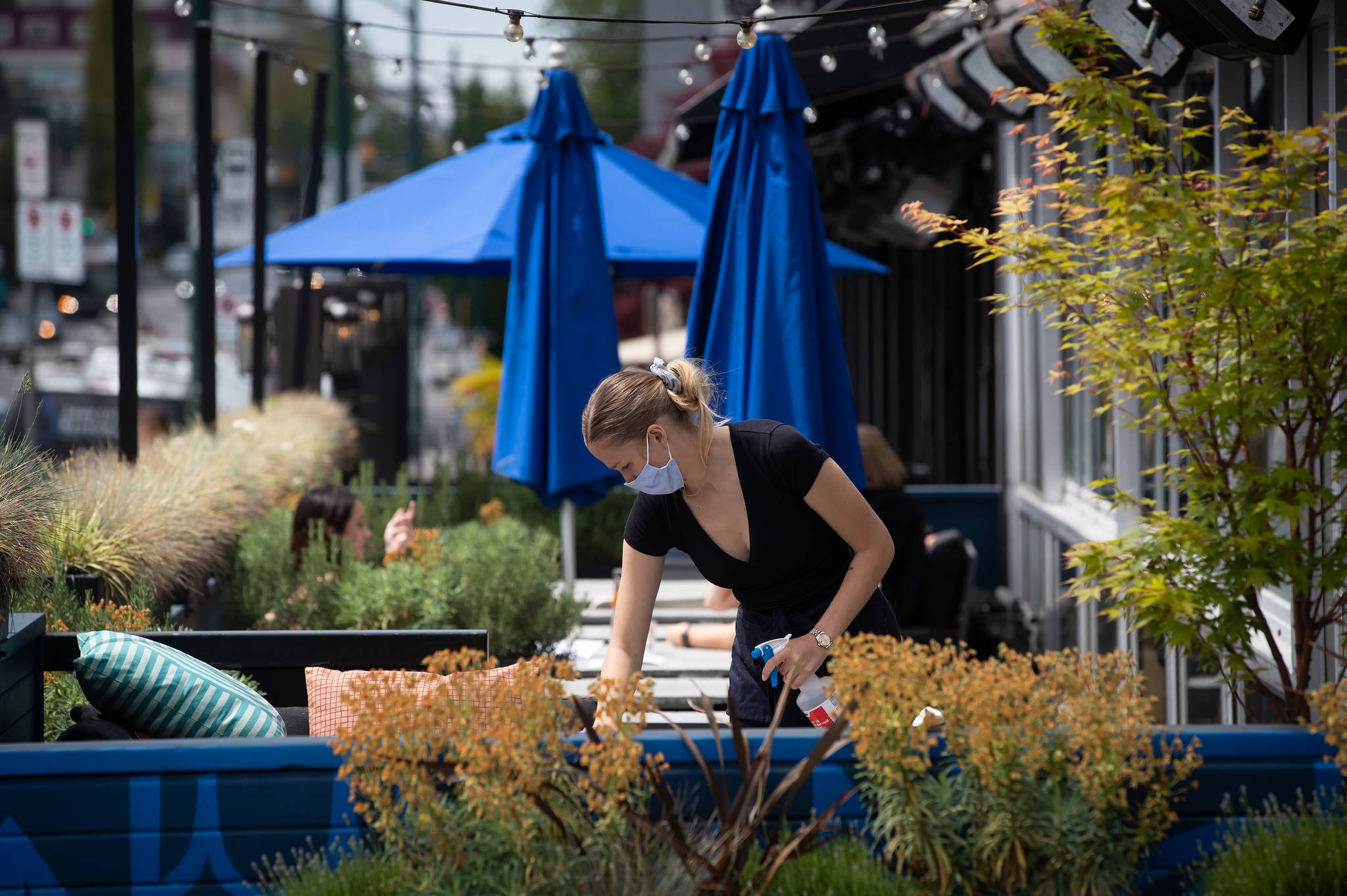 A server wears a face mask while cleaning a table on the patio at an Earls restaurant in Vancouver in May. A group of doctors and dentists are calling on the B.C. government to make masks mandatory. Photo: Darryl Dyck/The Canadian Press