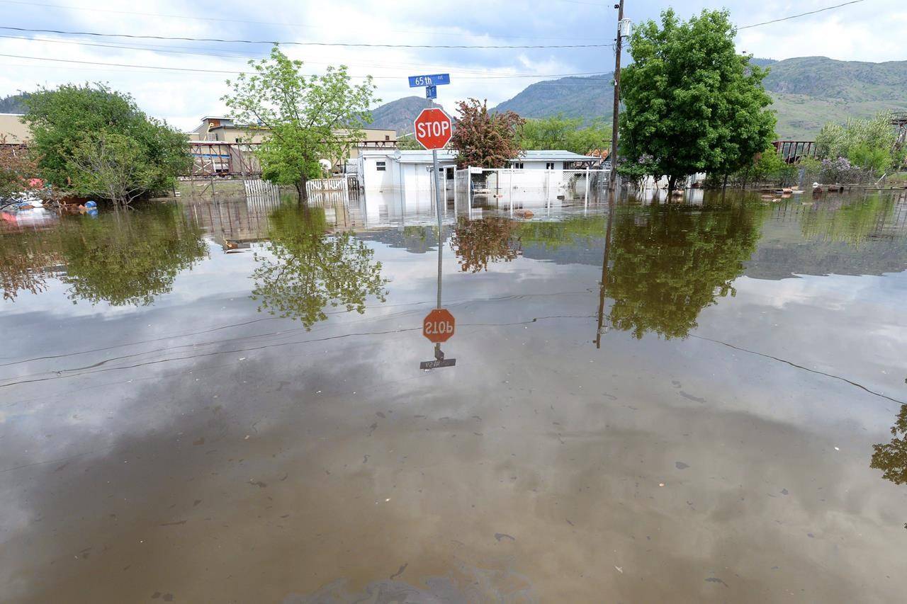 A stop sign is shown in a flooded intersection in Grand Forks, B.C., on May 17, 2018. A new report says provincial governments are not moving fast enough to protect homes and other buildings from the ravages of flooding. The report from the Intact Centre on Climate Adaptation at the University of Waterloo says on average provincial governments get a grade of C for flood preparedness. THE CANADIAN PRESS/Jonathan Hayward