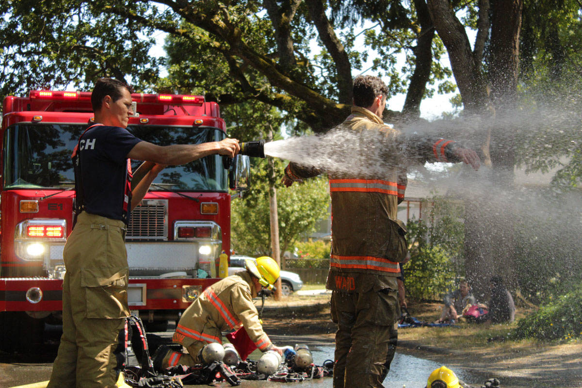 Firefighter Joel Anthony (left) helps fellow Saanich firefighter Josh Ward spray down his gear after extinguishing a house fire in the 500-block of Walter Avenue. (Devon Bidal/News Staff)