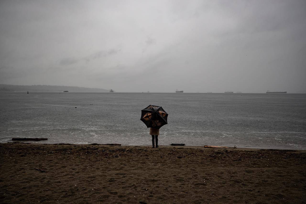 A person stands under an umbrella while looking out at English Bay as heavy rain falls, in Vancouver, B.C., Sunday, Oct. 11, 2020. THE CANADIAN PRESS/Darryl Dyck