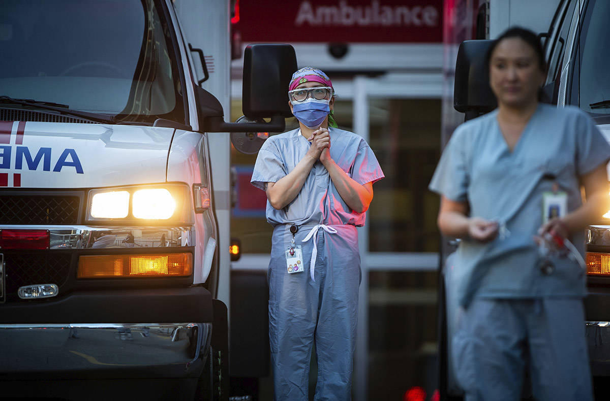 Healthcare workers at St. Paul’s Hospital acknowledge applause and cheers from people outside the hospital, as a convoy of first responders with lights and sirens activated parade past to show support for the hospital staff, in Vancouver, British Columbia, April 5, 2020. (Darryl Dyck/The Canadian Press via AP)