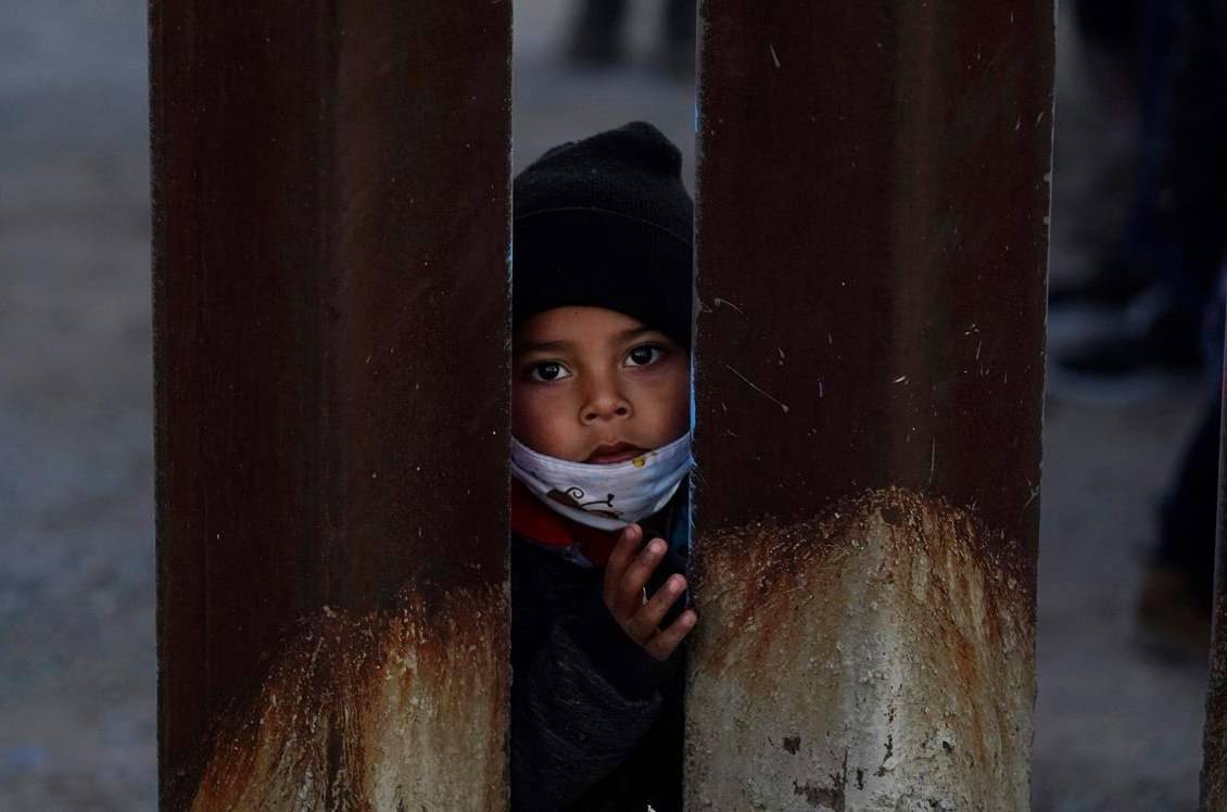 A young boy, part of several asylum seeking families participating in a Las Posadas event at the U.S.-Mexico border wall, peers into the U.S. from Agua Prieta, Mexico Tuesday, Dec. 15, 2020, seen from Douglas, Ariz. People on each side of the border celebrate Las Posadas as they have done for decades, a centuries-old tradition practiced in Mexico re-enacts Mary and Joseph's search for refuge in Bethlehem through songs, with several of the families attending stuck south of the border, their lives in limbo with U.S. proceedings suspended amid the COVID-19 pandemic. (AP Photo/Ross D. Franklin)