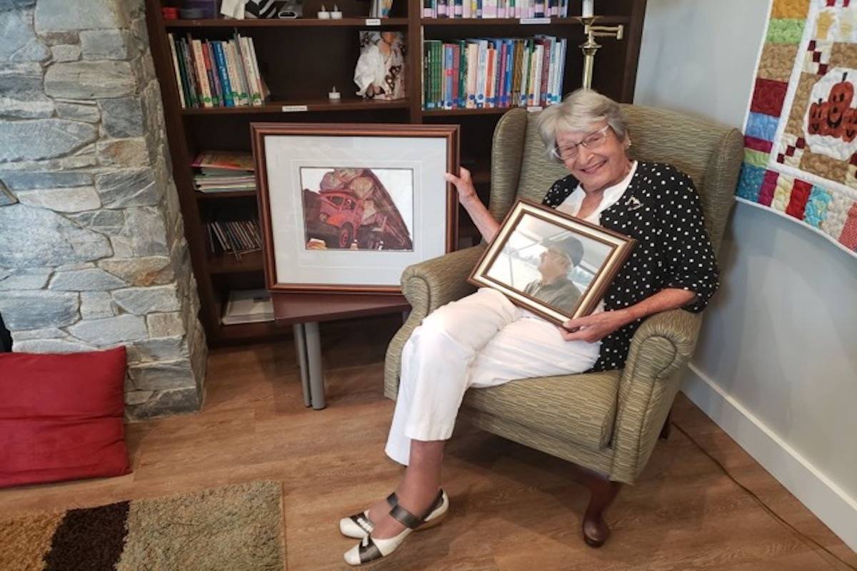 Joy Sharpe holds a picture of her late husband Ray while posing for a photograph with the Sybil Andrews painting ‘hauling’ before donating it to the Campbell River Hospice Society. (Submitted photo)