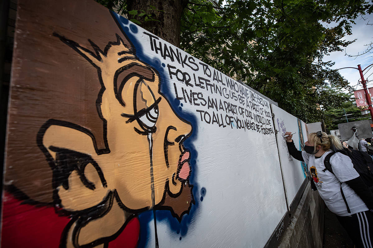 A woman writes a message on a memorial mural wall by street artist James “Smokey Devil” Hardy during a memorial to remember victims of illicit drug overdose deaths on International Overdose Awareness Day, in the Downtown Eastside of Vancouver, on Monday, August 31, 2020. THE CANADIAN PRESS/Darryl Dyck
