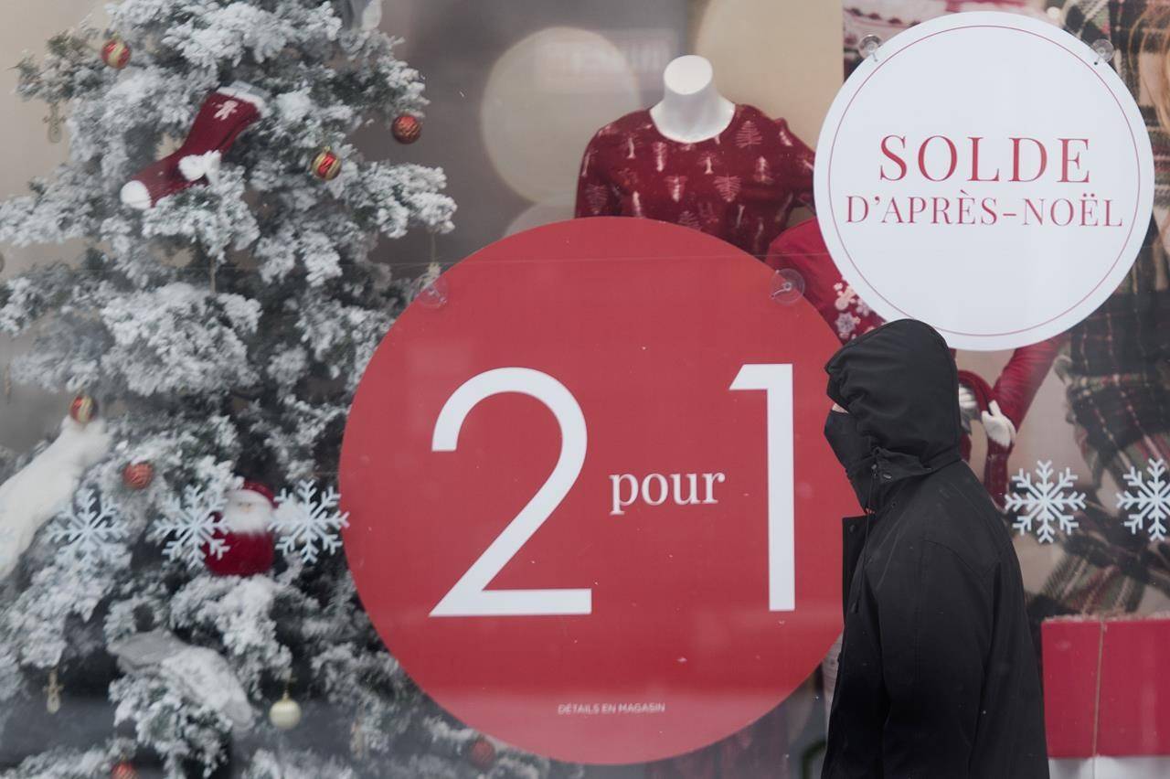 A man wears a face mask as he walks by a storefront window advertising after Christmas sales on Boxing Day in Montreal, Saturday, Dec. 26, 2020. Statistics Canada says retail sales climbed 1.3 per cent to $55.2 billion in November, rising for the seventh straight month. THE CANADIAN PRESS/Graham Hughes