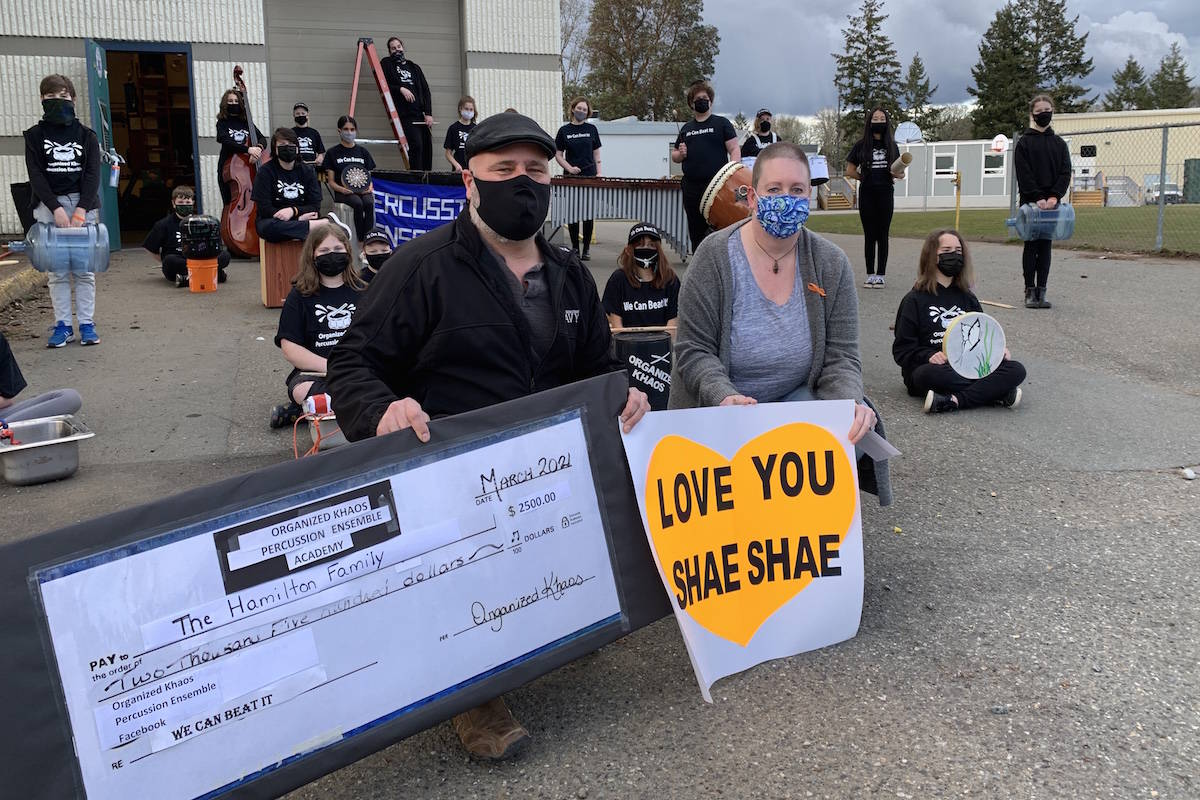 Allen and Lynn Hamilton accept a $2,500 donation from the Organized Khaos Percussion Ensemble (whose members are seen behind the couple) on March 9 at Spencer Middle School in Langford. The donation will go toward costs associated with staying in Vancouver, where the Hamiltons’ daughter is receiving leukemia treatments. (Jake Romphf/Black Press Media)