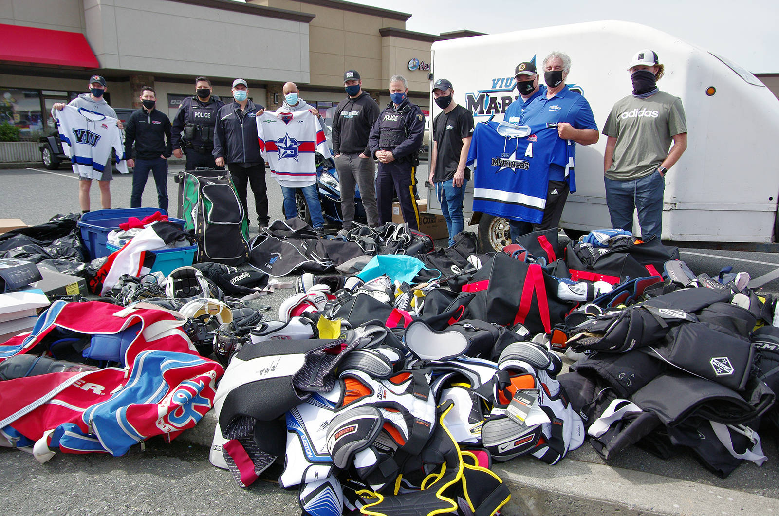 Nanaimo RCMP members and staff and team members with the VIU Mariners Hockey Club and staff with Kirby’s Source for Sports stand behind a pile of donated hockey gear that will be sent to outfit children and youths in Kinngait, Nunavut. (Chris Bush/News Bulletin)