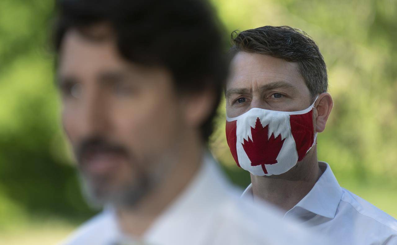 Local MP William Amos wear a Canadian flag mask as Prime Minister Justin Trudeau speaks during a news conference in Chelsea, Quebec. THE CANADIAN PRESS/Adrian Wyld