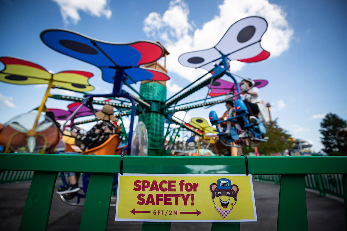 FILE – A sign reminding guests to stay 2 metres apart is seen on a fence as people ride an attraction at Playland amusement park at the Pacific National Exhibition, in Vancouver, on Friday, July 10, 2020. THE CANADIAN PRESS/Darryl Dyck