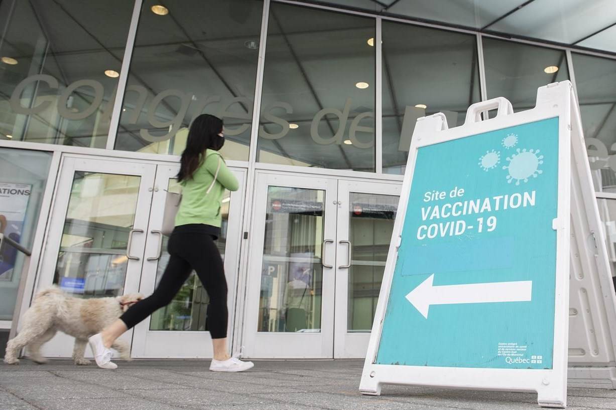 A woman and dog walk by a sign at a COVID-19 vaccination site in Montreal, Sunday, July 4, 2021. The federal government is expecting to receive 3.7 million more doses of COVID-19 vaccines this week which will make the total COVID-19 vaccine deliveries top 53.7 million doses by the end of the week. THE CANADIAN PRESS/Graham Hughe