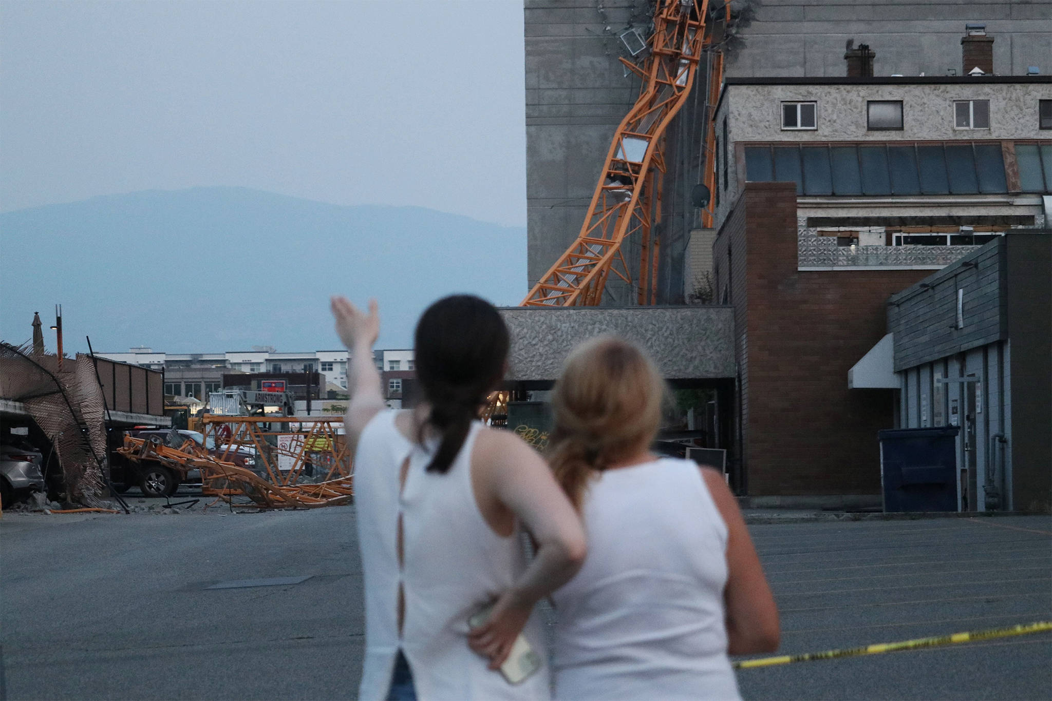Two women look at the wreckage on the morning of Tuesday, July 13, after a crane collapsed in downtown Kelowna the day previous. (Aaron Hemens/Capital News)