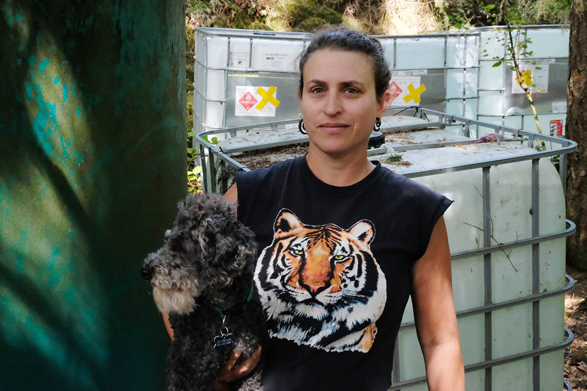 Miranda Aloma (with dog Sherlock) stands in front of what she jokingly calls her water tank ghetto. She has already used up the auxiliary water she’d reserved in the spring, and is relying on water deliveries earlier than she ever has before. Three tanks in the back are not-potable; she rigs up hoses and buckets and uses that water for plants. (Zoe Ducklow/News Staff)