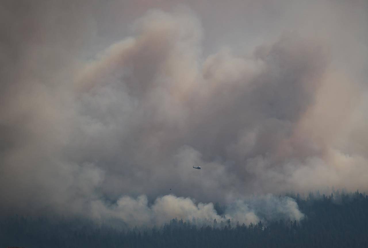 A helicopter with a water bucket flies past the Tremont Creek wildfire burning on the mountains above Ashcroft, B.C., on Friday, July 16, 2021. THE CANADIAN PRESS/Darryl Dyck