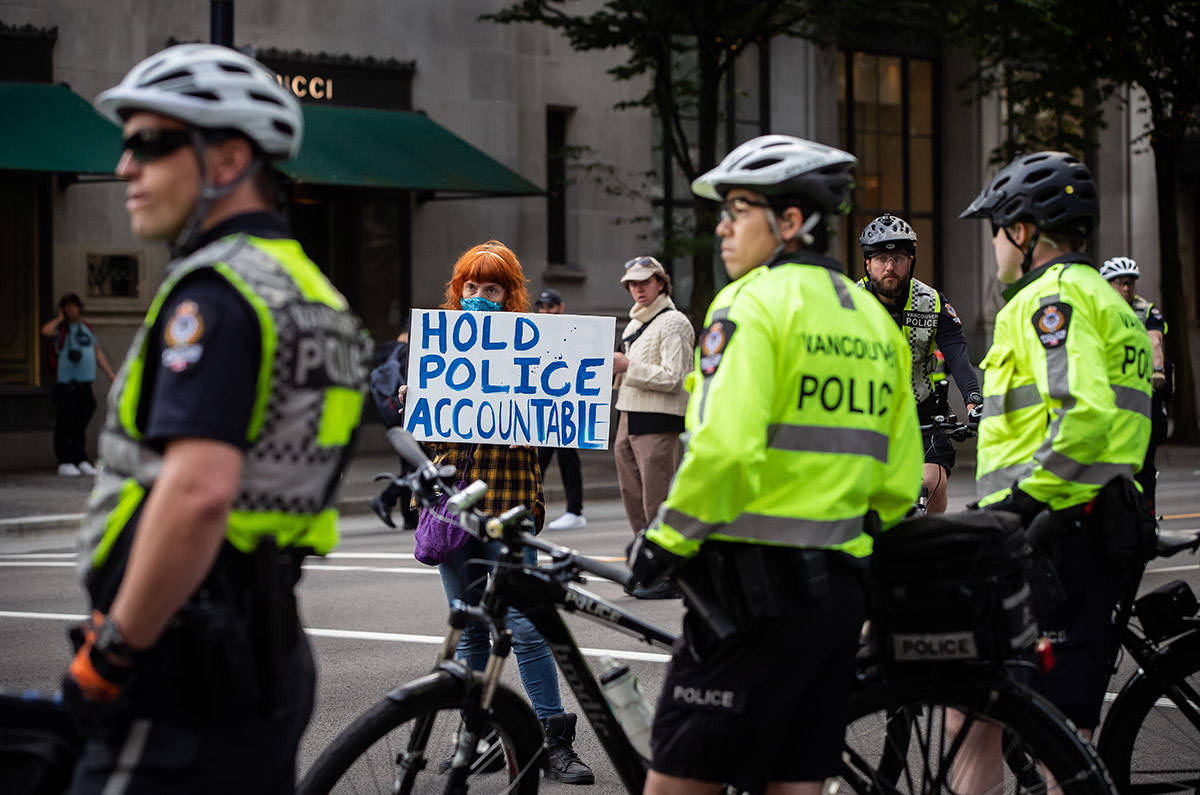 A woman holds a sign reading “Hold Police Accountable” near police officers watching as thousands of people gather for a peaceful demonstration in support of George Floyd and Regis Korchinski-Paquet and protest against racism, injustice and police brutality, in Vancouver, on Sunday, May 31, 2020. Photo: Darryl Dyck/The Canadian Press