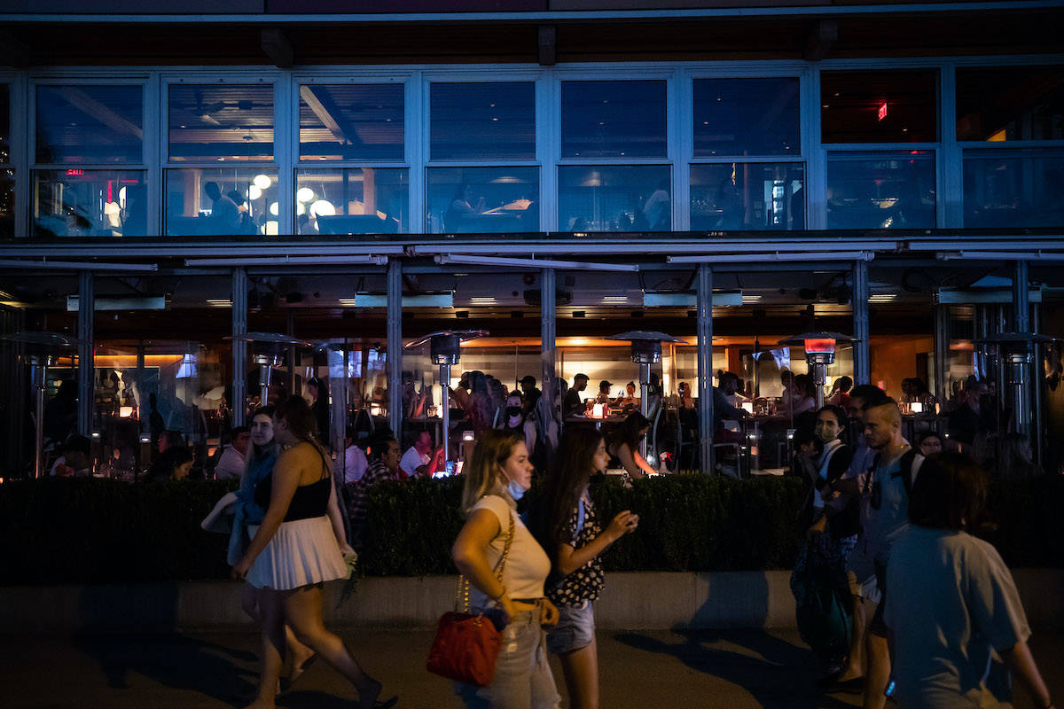 People walk past patrons inside a restaurant and on an outdoor patio at English Bay, in Vancouver, B.C., on Monday, June 21, 2021. THE CANADIAN PRESS/Darryl Dyck