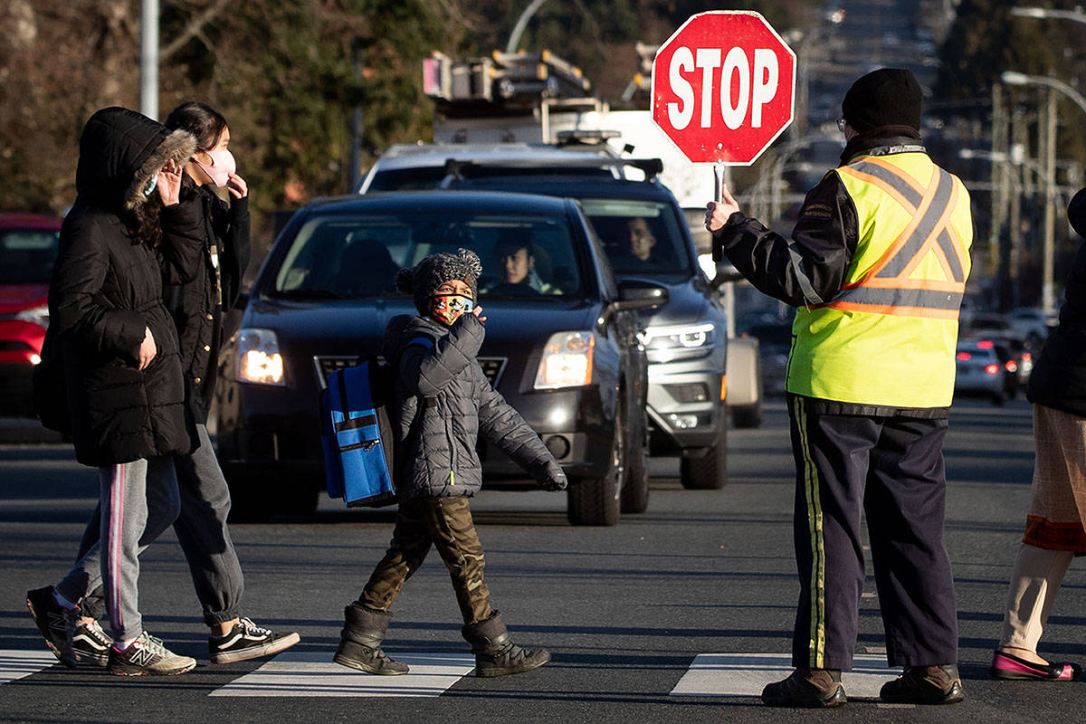 A crossing guard stops traffic as students wearing face masks to curb the spread of COVID-19 arrive at Ecole Woodward Hill Elementary School, in Surrey, B.C., on Tuesday, February 23, 2021. A number of schools in the Fraser Health region, including Woodward Hill, have reported cases of the B.1.7.7 COVID-19 variant first detected in the U.K. THE CANADIAN PRESS/Darryl Dyck