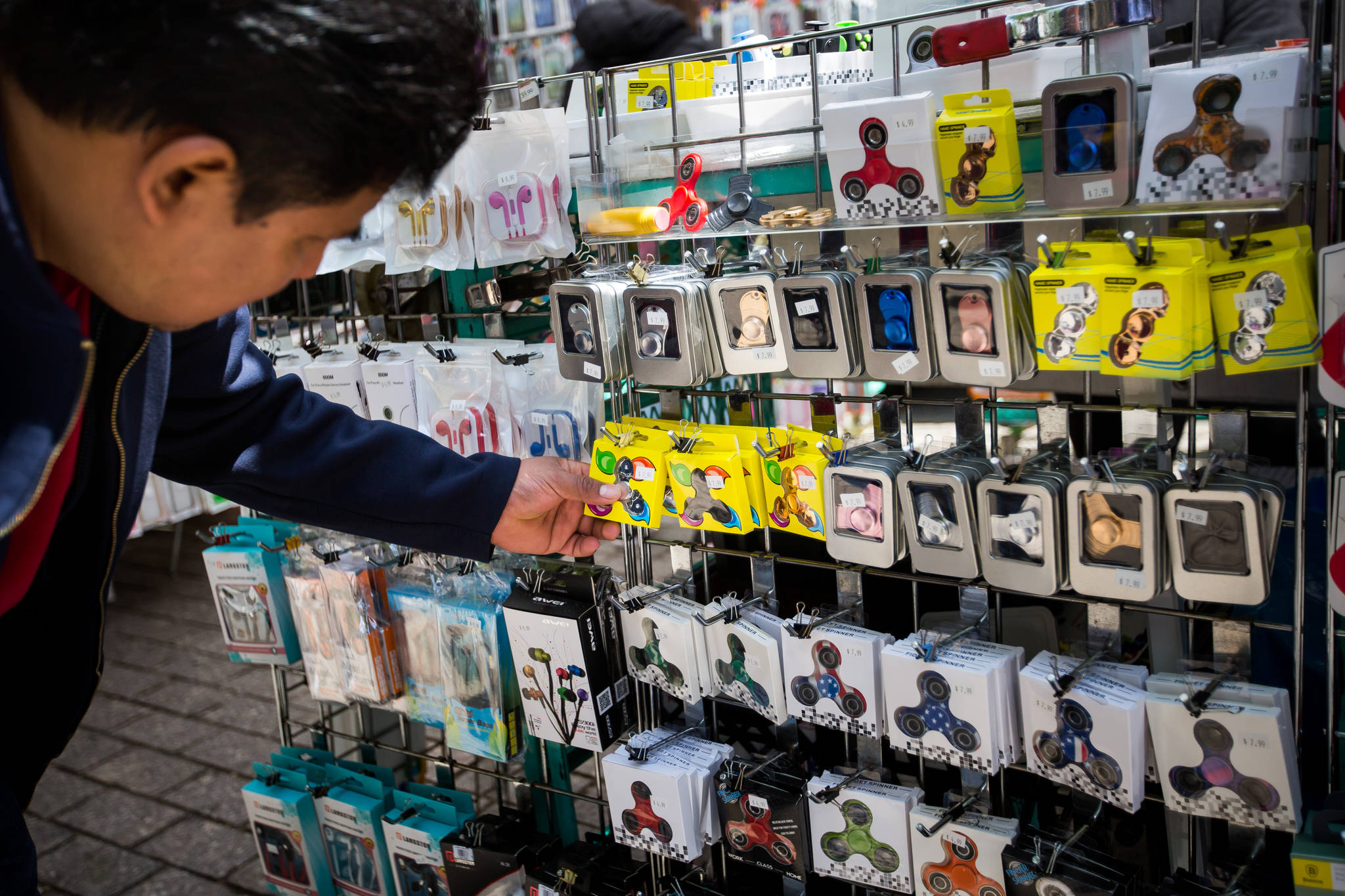 A shopper browses fidget spinners displayed for sale by a street vendor in New York, U.S., on Friday, May 12, 2017. The fidget spinner is a toy that sits like a propeller on a person’s finger, with blades that spin around a bearing. MUST CREDIT: Photo by Michael Nagle/Bloomberg.