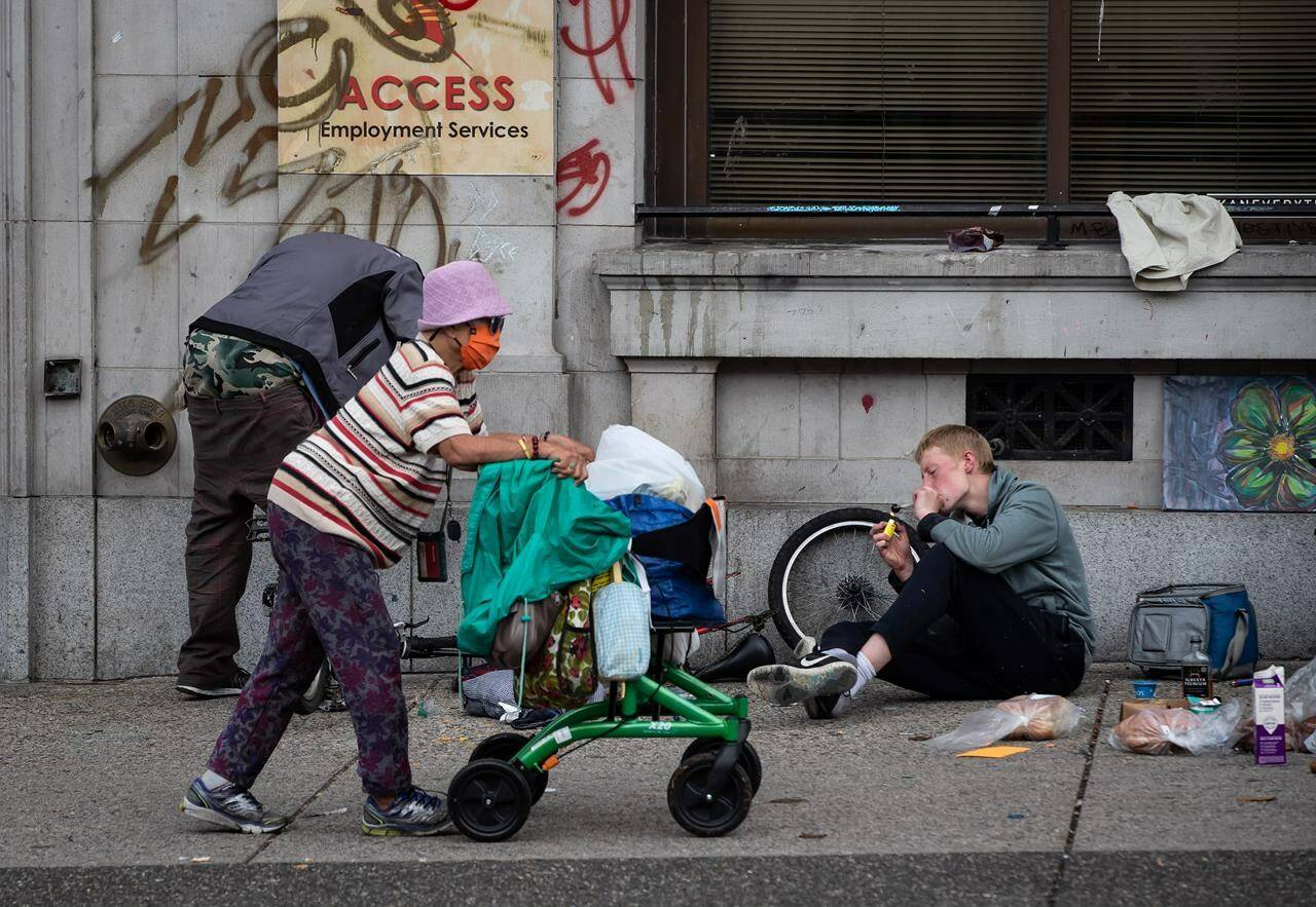 A woman walks past a person using a glass pipe to smoke drugs in the Downtown Eastside of Vancouver, on International Overdose Awareness Day on Tuesday, August 31, 2021. THE CANADIAN PRESS/Darryl Dyck