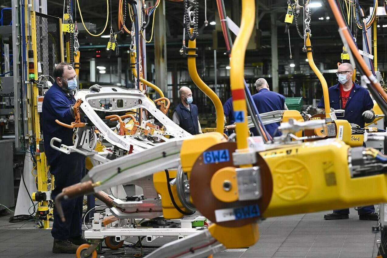 GM workers use human assistance automation on vehicle doors at the General Motors assembly plant during the COVID-19 pandemic in Oshawa, Ont., on Friday, March 19, 2021. More than 880,000 Canadians work in industries at risk of decline or closure in the global transition to clean energy, a new analysis says. THE CANADIAN PRESS/Nathan Denette