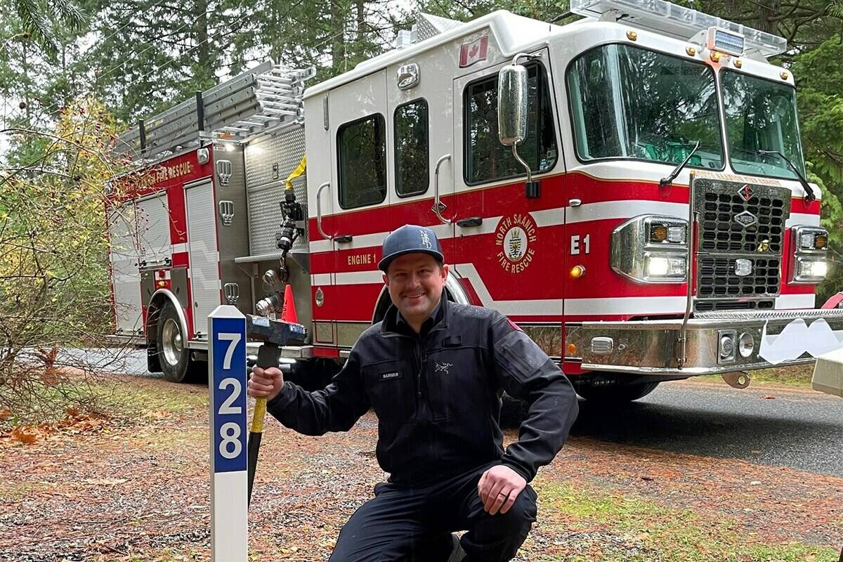 A North Saanich firefighter poses alongside a reflective address sign, which helps emergency crews save time when searching for an address in the dark. (Courtesy of North Saanich Fire Department)