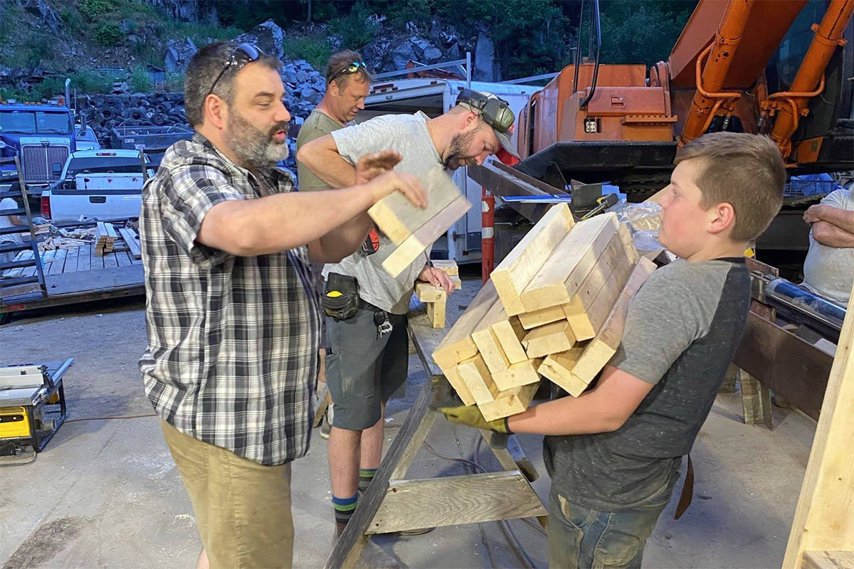 Matthew Lasser steadies himself as Jim Lasser loads him up with wood during a building party to make beds for local firefighters, as Samuel Masterton and Keith Lasser work in the background. (Submitted/Stephanie Hooker)