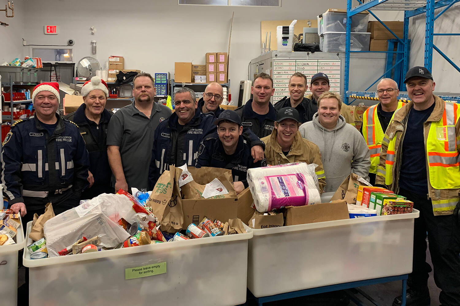 Saanich Peninsula firefighters join staff from the Saanich Peninsula Lions Food Bank in showing off donations to the Peninsula Firefighters Christmas Food Drive in 2019. The food drive returns next month after being cancelled in 2020 due to COVID-19. (Photo courtesy Tyson Elder)