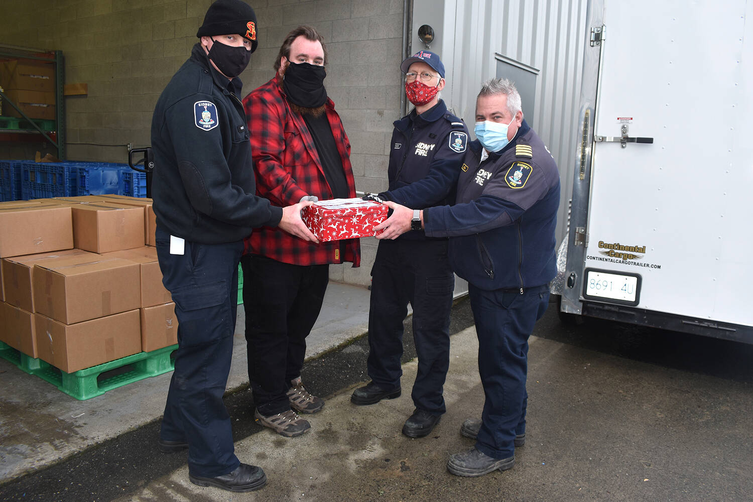 (In uniform from left) Sidney Volunteer Fire Department firefighter Craig Pelton, Lt. Rick Toogood and Deputy Fire Chief Mike Harman hand Tyson Elder of the Saanich Peninsula Lions Food Bank more than $14,000 in cash donations collected Dec. 11 during the Peninsula Firefighters Christmas Food Drive. (Wolf Depner/News Staff)