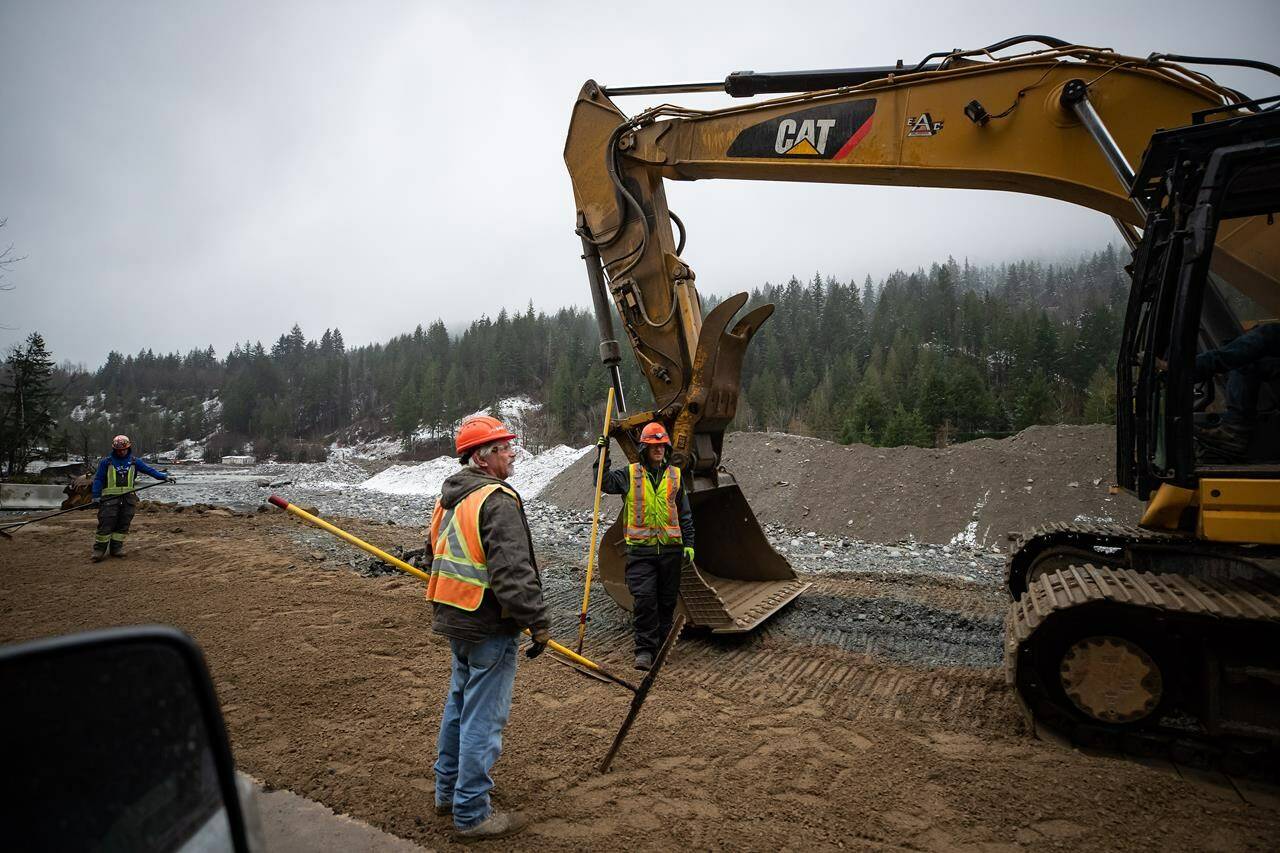 Construction workers stand in the northbound lanes of the Coquihalla Highway where a massive section of the separate southbound lanes was washed away by flooding last month near Othello, northeast of Hope, B.C., on December 10, 2021. THE CANADIAN PRESS/Darryl Dyck