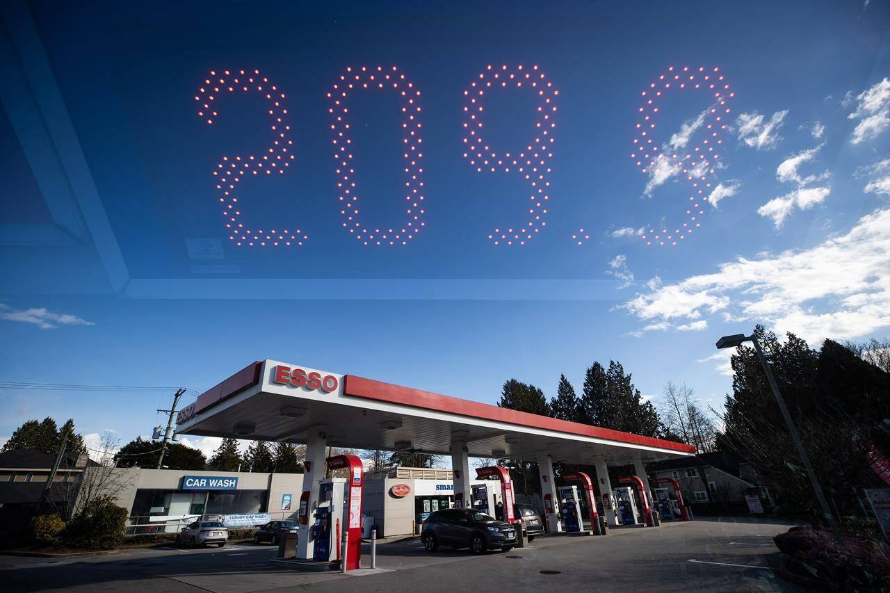 In this double exposure photograph, a sign displays the price of a litre of regular grade gasoline as people fuel up their vehicles at an Esso gas station, in Vancouver, on Tuesday, March 8, 2022. THE CANADIAN PRESS/Darryl Dyck