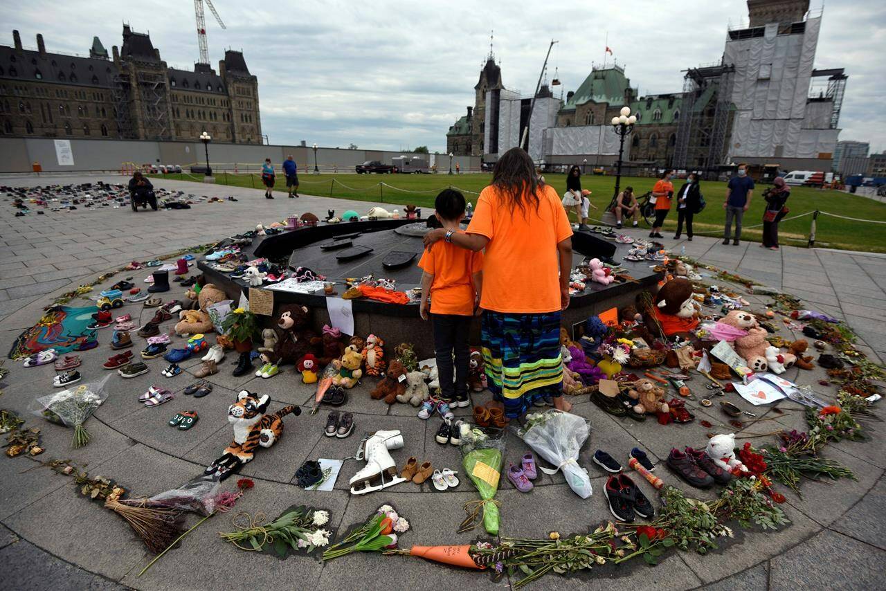 Judy Sackaney and her grandson Creedence, 10, stand in front of an honour staff with tobacco ties at the Centennial Flame after participating in a Pipe Ceremony to honour the 215 children whose remains were found at the grounds of the former Kamloops Indian Residential School at Tk’emlups te Secwépemc First Nation in Kamloops, B.C., on Parliament Hill in Ottawa, on Saturday, June 5, 2021. Government officials spent weeks trying to figure out how best to remove a memorial on Parliament Hill for Indigenous children who died and went missing from residential schools, with an initial recommendation to try and have it taken down in a ceremony before last fall’s federal election. THE CANADIAN PRESS/Justin Tang