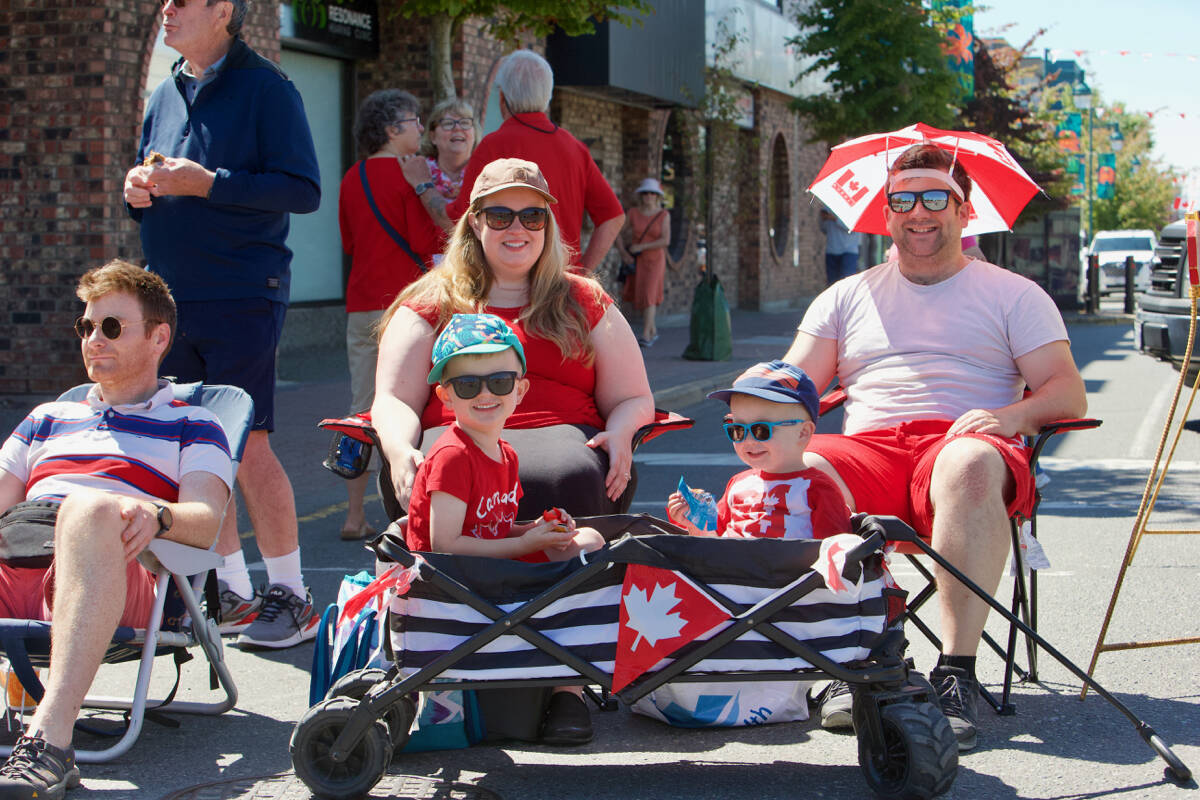 A family dressed in Canada Day garb sits along Beacon Avenue Friday to take in Sidney’s Canada Day Parade. The parade returned in person after a two years due to the pandemic. (Justin Samanski-Langille/News Staff)