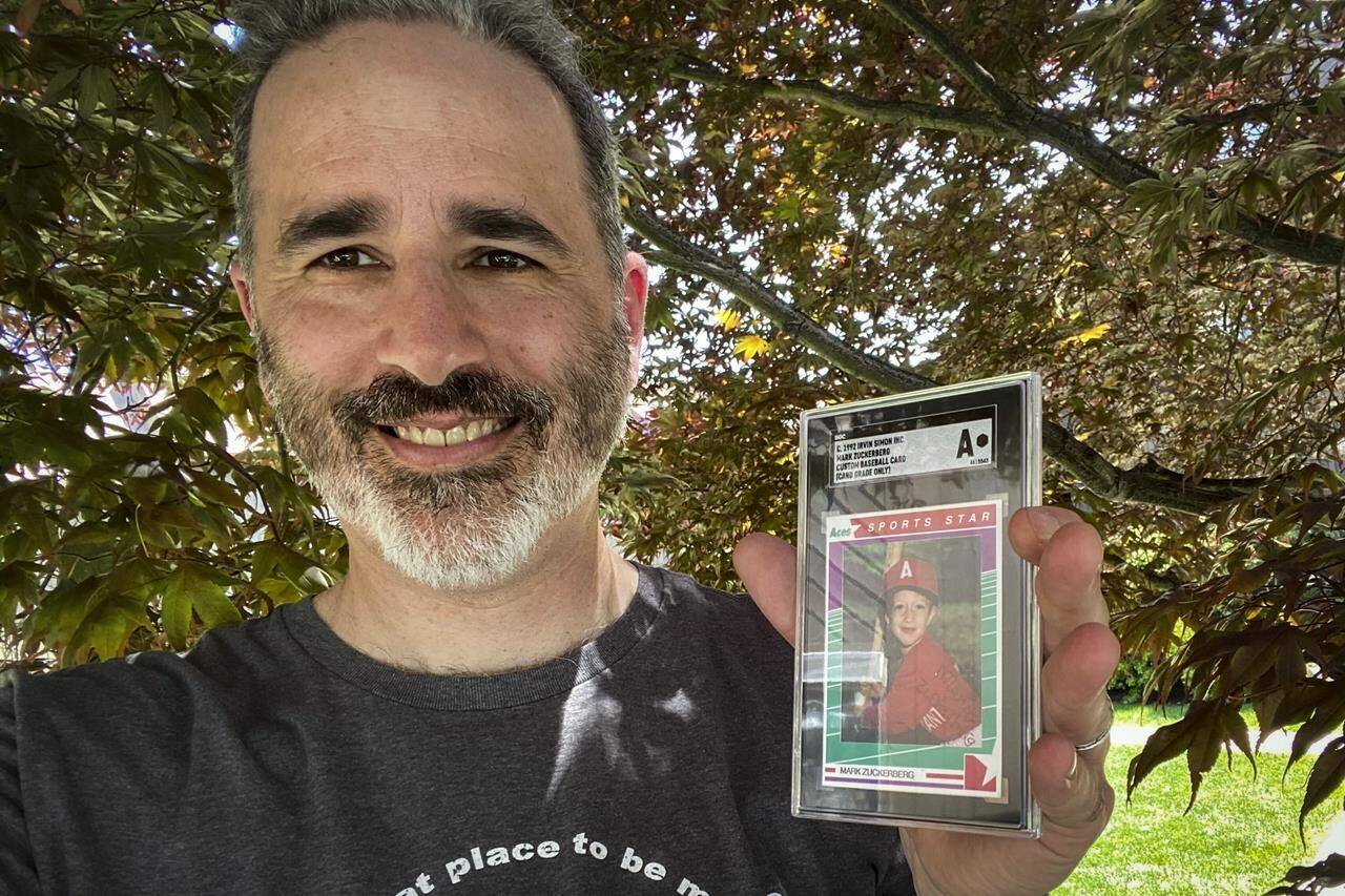 This photo provided on Wednesday, Aug. 3, 2022, shows Allie Tarantino holding a baseball card featuring a very young Mark Zuckerberg grinning in a red jersey and gripping a bat. For 30 years Tarantino kept the baseball card filed it away in his basement, not knowing Zuckerberg would someday become a household name. (Shira Tarantino via AP)