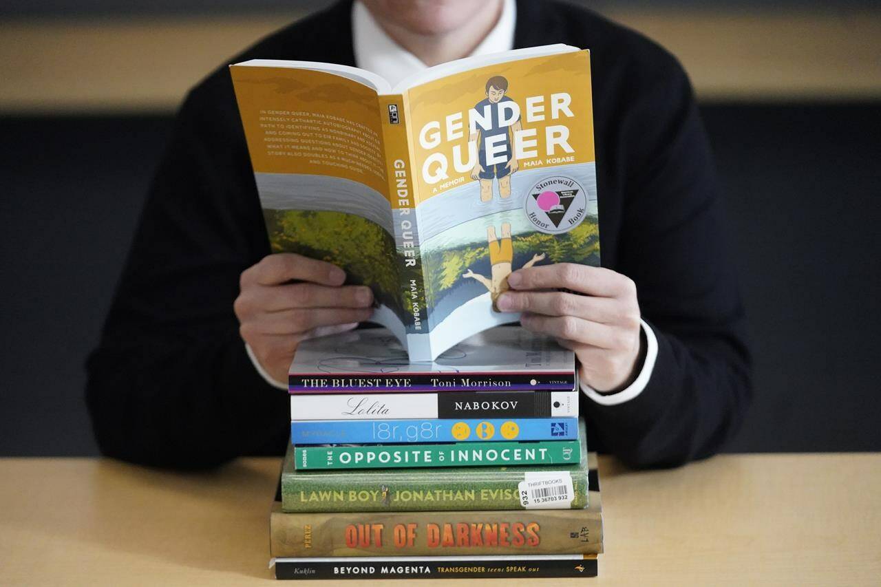 FILE - Amanda Darrow, director of youth, family and education programs at the Utah Pride Center, poses with books that have been the subject of complaints from parents in Salt Lake City on Dec. 16, 2021. The wave of attempted book banning and restrictions continues to intensify, the American Library Association reported Friday. Numbers for 2022 already approach last year’s totals, which were the highest in decades. (AP Photo/Rick Bowmer, File)