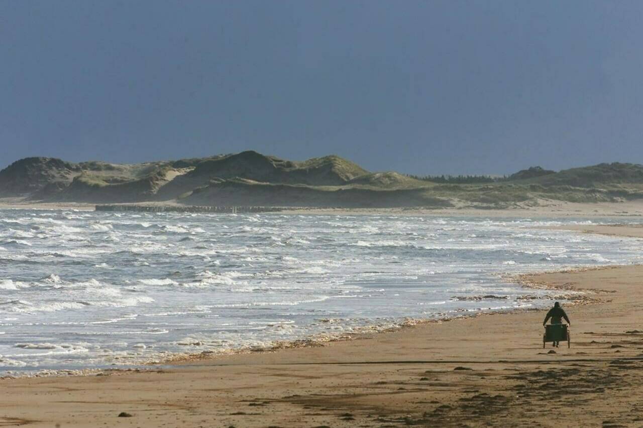 An unidentified man pulls a hand cart along the beach in Prince Edward Island National Park, near Stanhope, on Friday, Oct. 25, 2002. Parks Canada says the scale of sand dune erosion at beaches in Prince Edward Island National Park due to post-tropical storm Fiona is “shocking.” THE CANADIAN PRESS/Andrew Vaughan