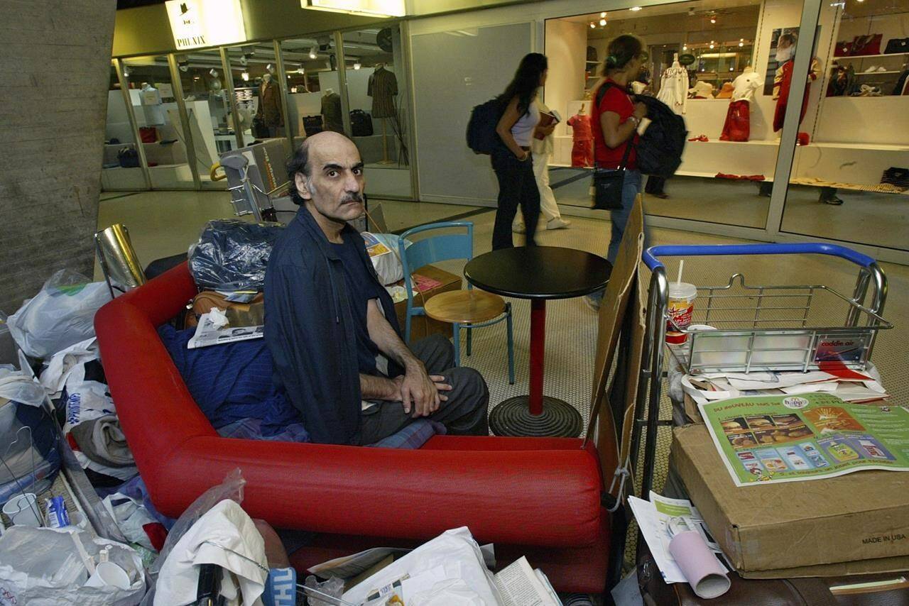 FILE - Merhan Karimi Nasseri sits among his belongings at Terminal 1 of Roissy Charles De Gaulle Airport, north of Paris on Aug. 11, 2004 . An Iranian man who lived for 18 years in Paris’ Charles de Gaulle Airport and inspired the Steven Spielberg film “The Terminal” died Saturday, Nov. 12, 2022 in the airport, officials said. Merhan Karimi Nasseri died after a heart attack in the airport’s terminal 2F around midday, according an official with the Paris airport authority. Police and then a medical team treated him but were not able to save him, the official said. (AP Photo/Michel Euler, File)
