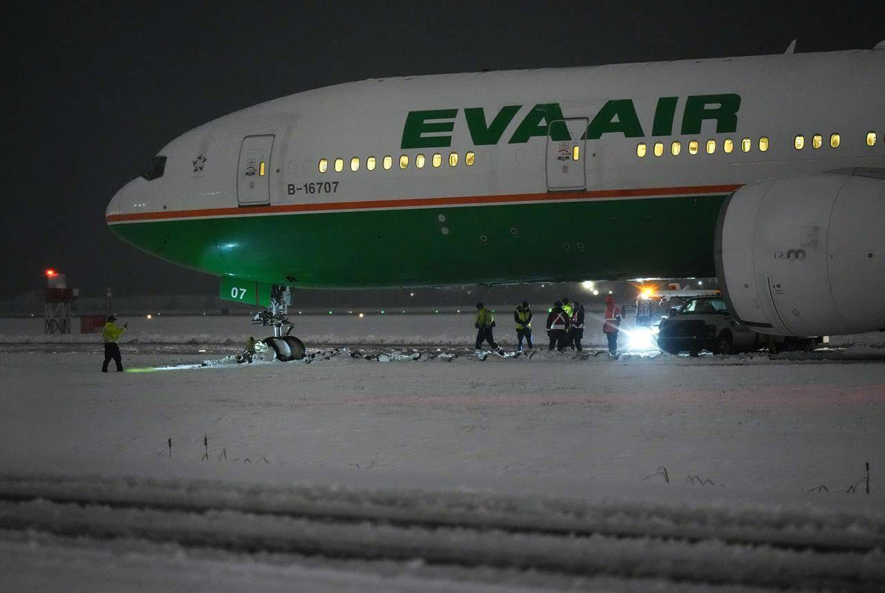 Workers are seen around an EVA Air Boeing 777 aircraft that went off a taxiway onto soft ground after landing at Vancouver International Airport from Taipei during a snowstorm during the early morning hours of Wednesday, Nov. 30, 2022. Nobody was injured and passengers were taken off the plane and shuttled to the terminal on buses after being stuck onboard for three hours. Snowfall, winter storm and arctic outflow warnings were in effect for most of British Columbia as a powerful storm packing frigid winds moved through the province. THE CANADIAN PRESS/Darryl Dyck